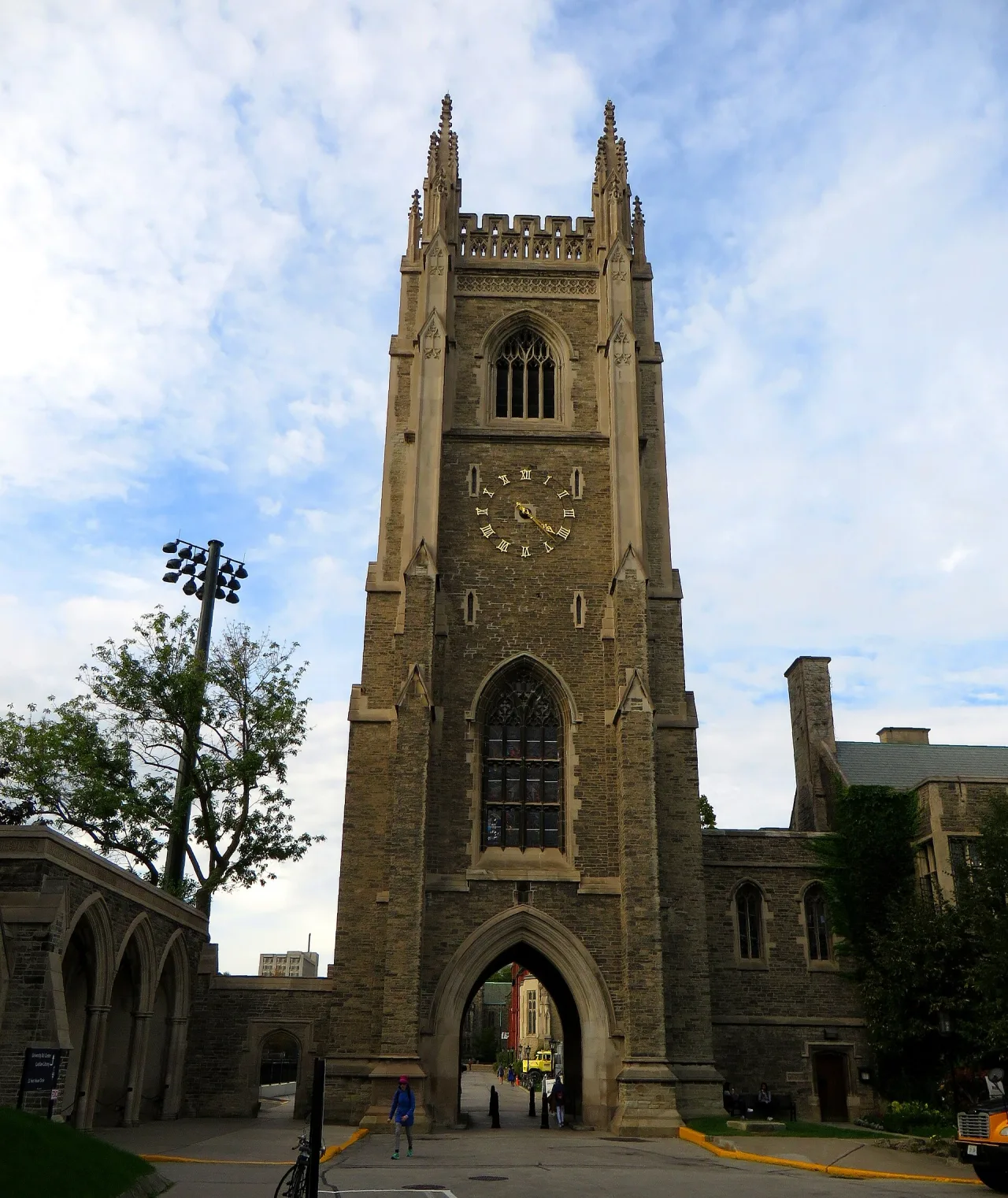 The tall stone Gothic tower with a gold-numbered clock face and an arched gateway at its base, under a blue sky with clouds.