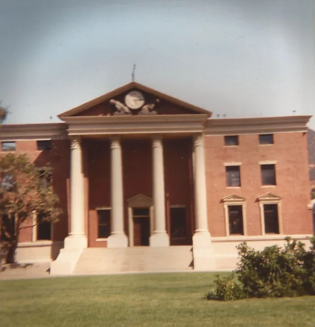Red brick courthouse with white columns, a pediment clock and a lawn in front, photographed on the studio backlot.