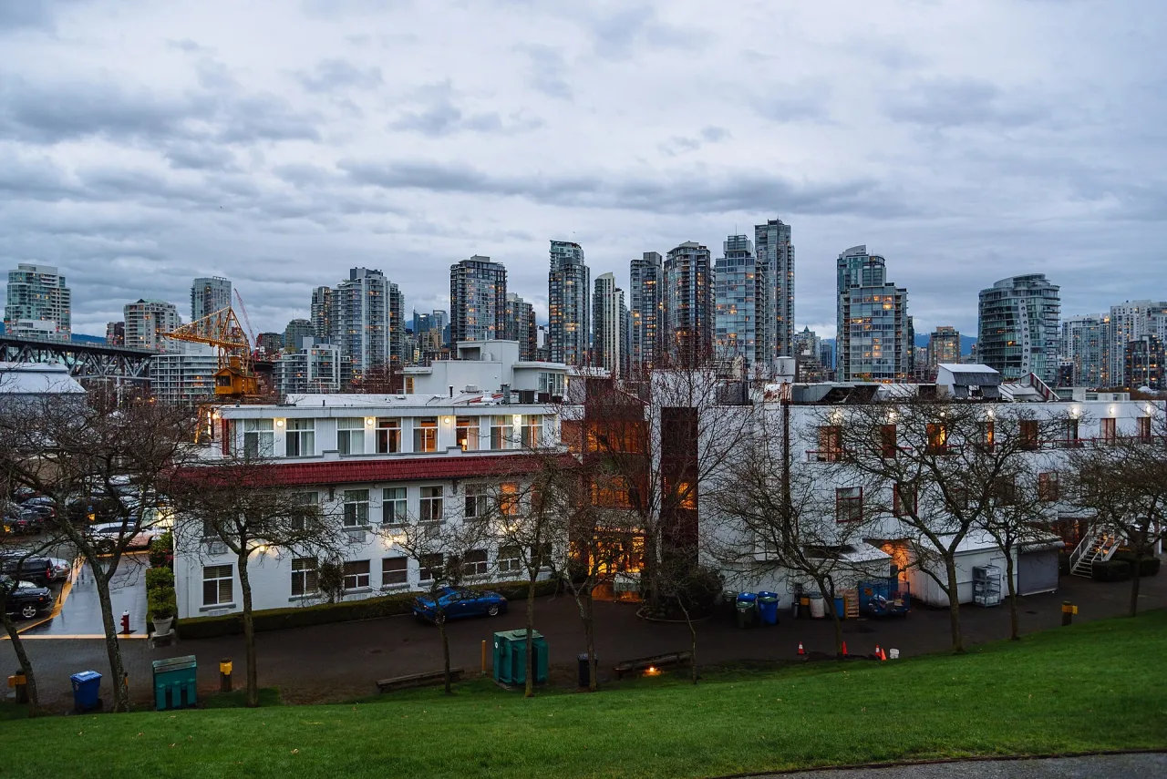 Vancouver's downtown towers at dusk under heavy cloud, seen across low buildings and a grassy slope