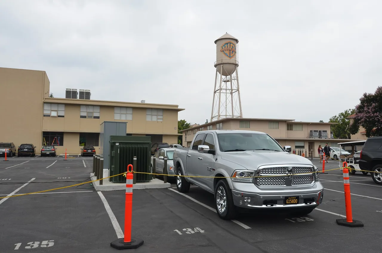 The Warner Bros. water tower rising above studio buildings and a car park on the Burbank lot, under an overcast sky.