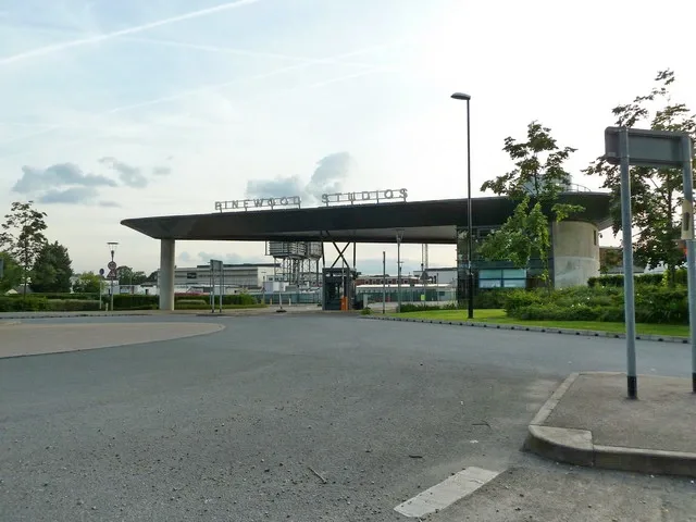The main entrance to Pinewood Studios, a flat canopy with the studio name in letters on top, seen from the road under a partly cloudy sky.