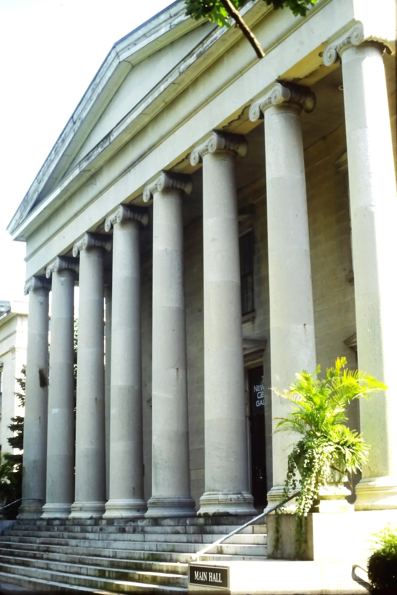 Greek Revival building with a row of tall stone columns and a pediment, reached by wide steps, with a Main Hall sign at the foot.