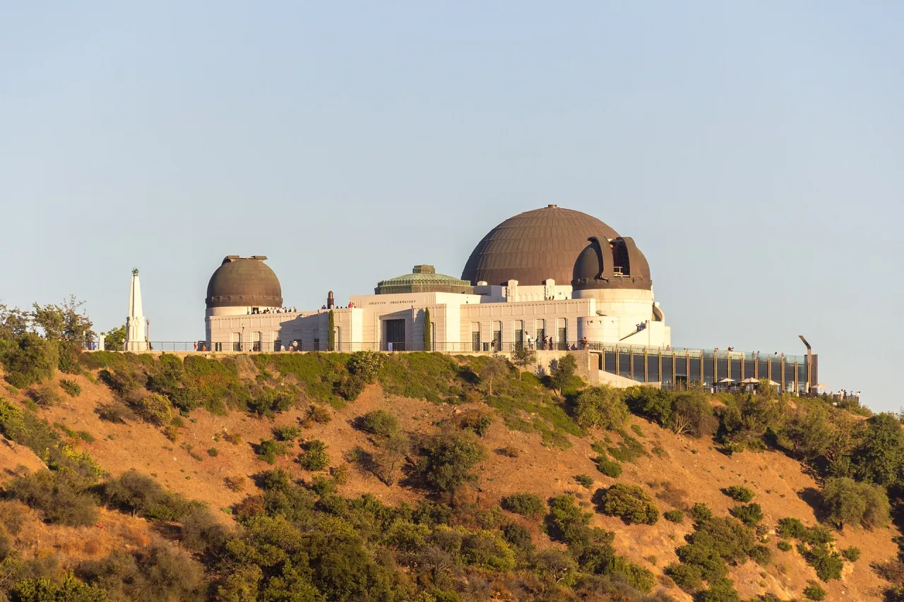 The white domed observatory on a dry hillside above Los Angeles in warm evening light, with visitors on its terrace.