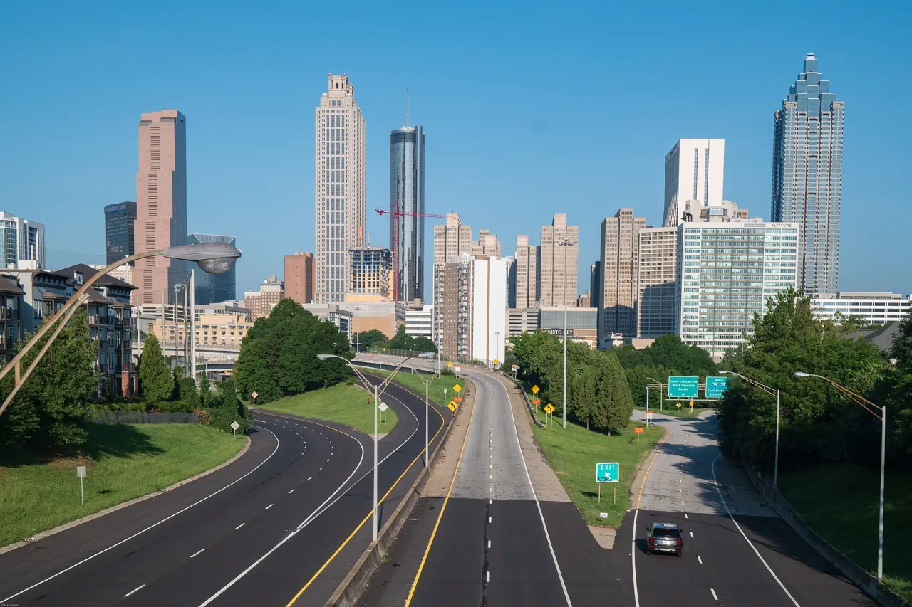 Downtown Atlanta skyline in clear sunshine, seen from a bridge over a nearly empty multi-lane road.