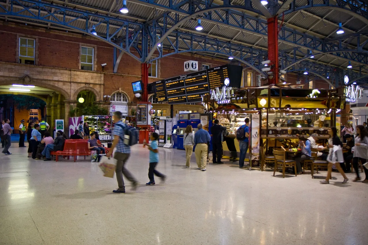 The busy concourse of Marylebone station under its blue iron roof, with travellers, departure boards and a cafe kiosk.