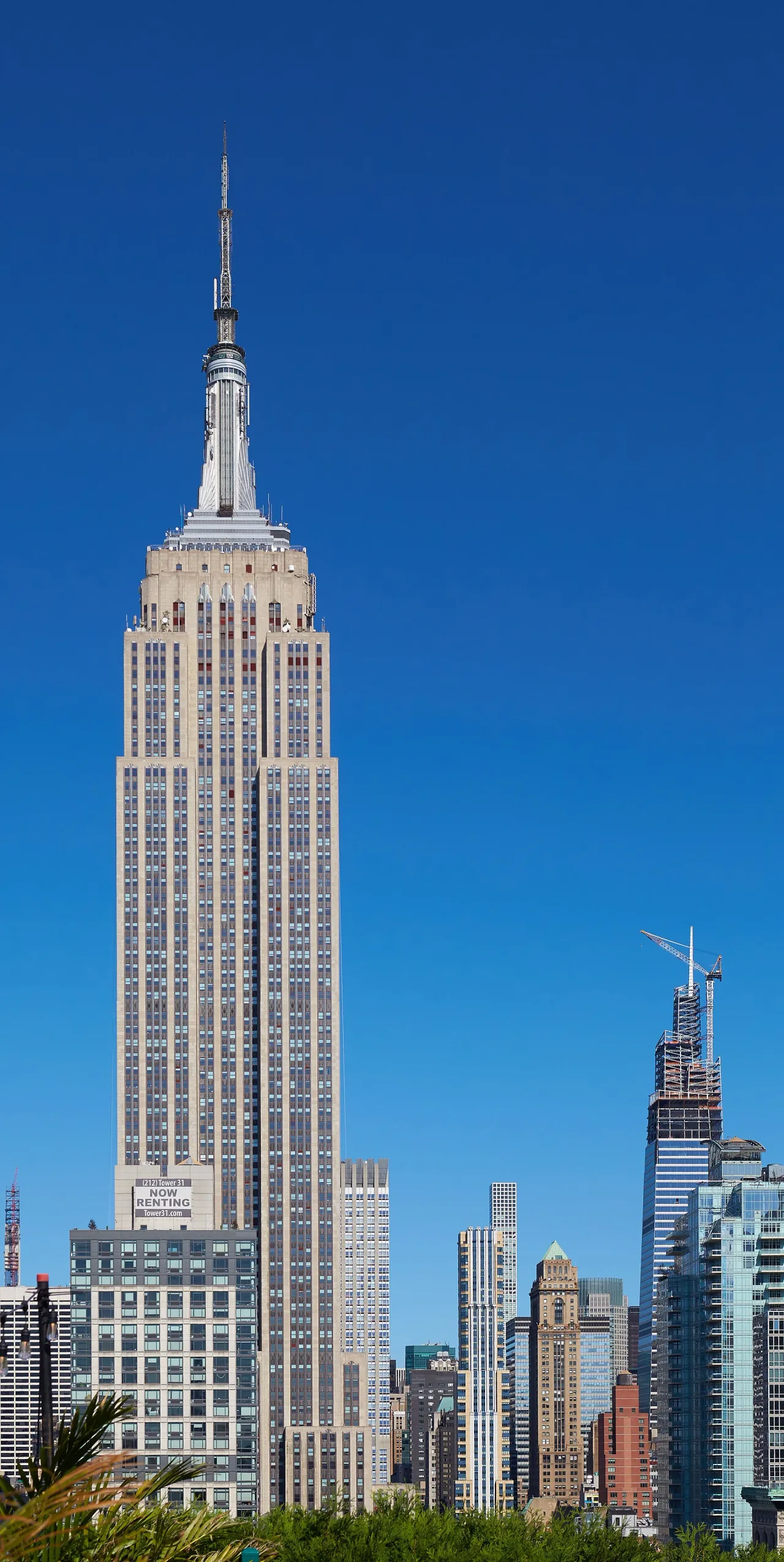 The Empire State Building rising with its tall spire against a clear blue sky, surrounded by smaller Manhattan towers.
