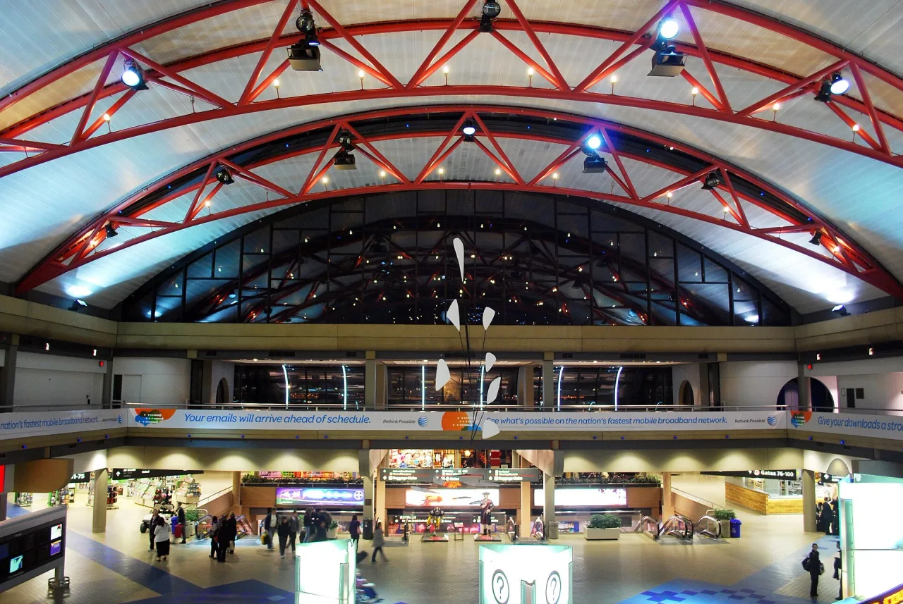 Inside the airside terminal at Pittsburgh International Airport, with a red steel-arched glass roof above a busy concourse of shops and travellers.
