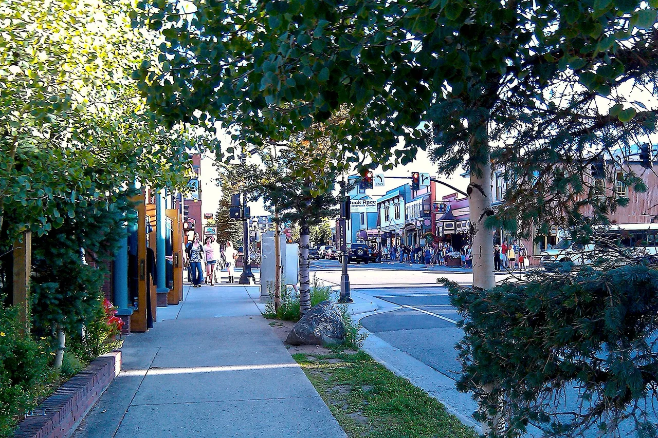 A street of low historic buildings in a mountain town, with snow-dusted peaks rising behind.