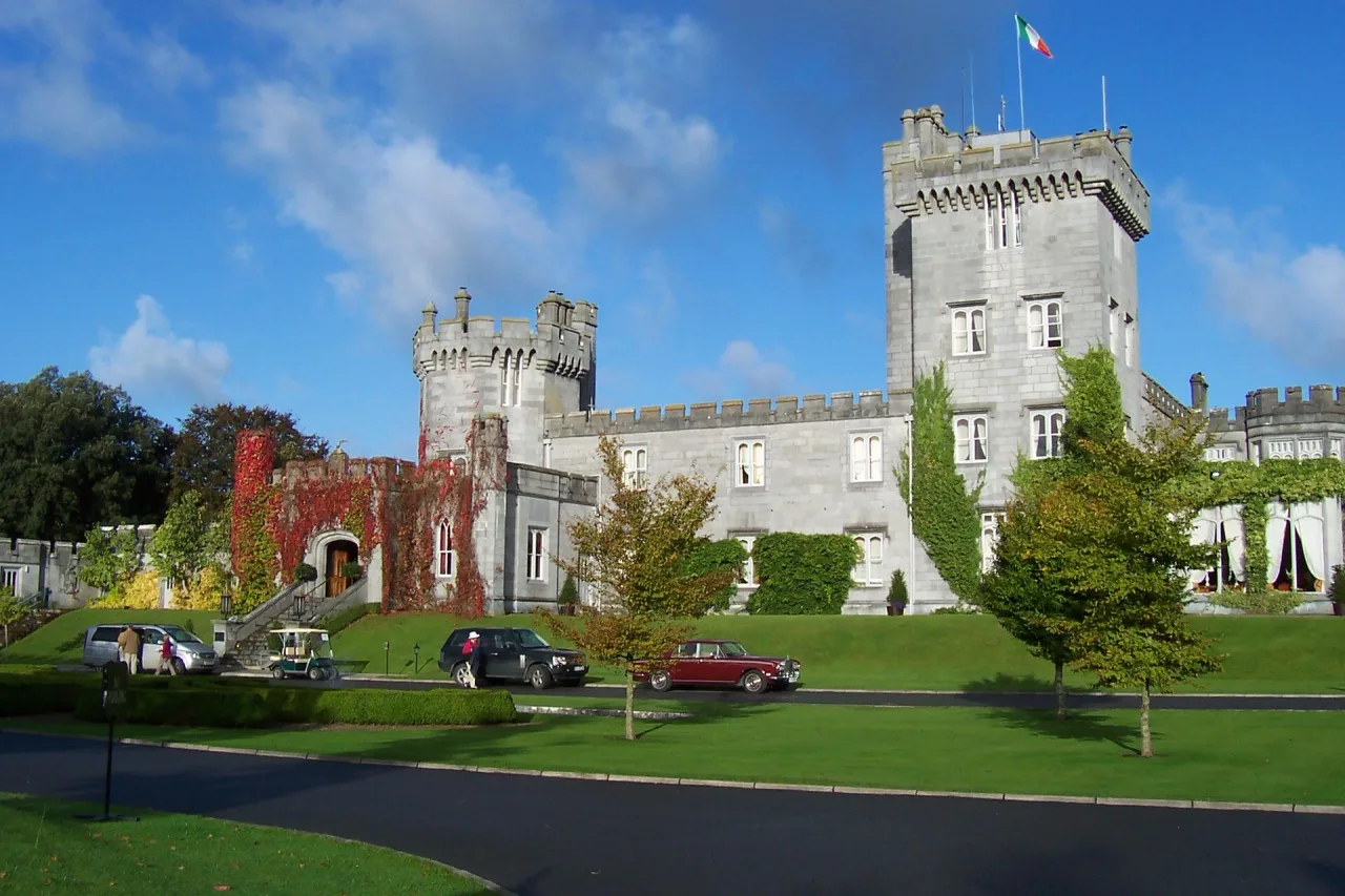 Grey stone castle with battlements and a square tower, partly covered in red and green ivy, above a lawn under a blue sky.