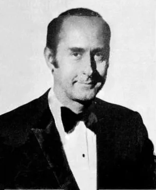 Black and white studio portrait of a man with receding dark hair in a velvet-lapelled dinner jacket and bow tie