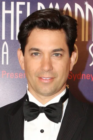 Adam Garcia in a black dinner jacket and bow tie, with dark swept hair, smiling slightly at the camera.