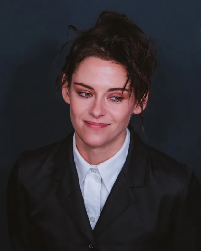 Head and shoulders photograph of a woman with dark hair pinned up, wearing a dark jacket over a white collared shirt, glancing to one side with a slight smile.
