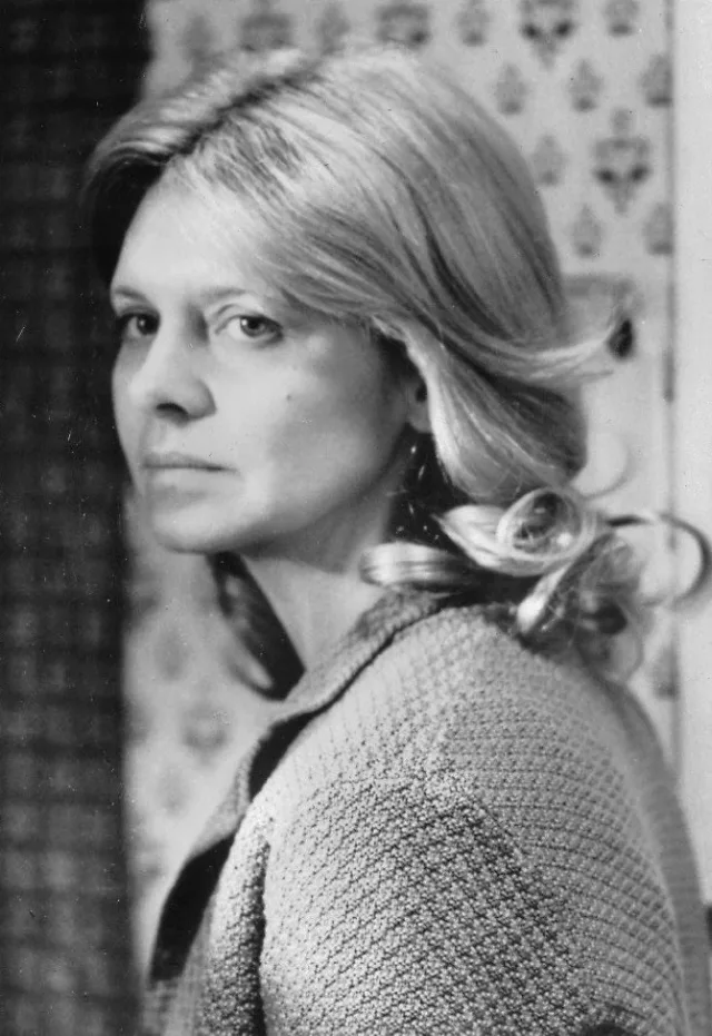 Black and white portrait of a woman with shoulder-length fair hair, looking back over her shoulder in a knitted cardigan