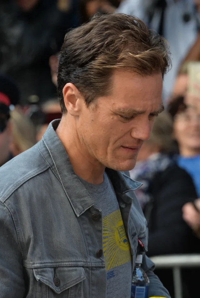 Michael Shannon in a grey denim jacket, looking down, with a crowd behind him at a film festival.