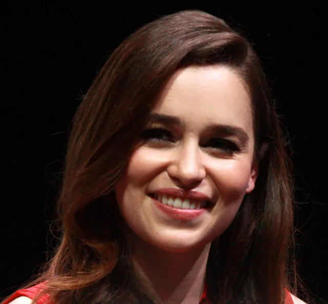Smiling woman with long brown hair swept to one side, in a red top, photographed against a black background.