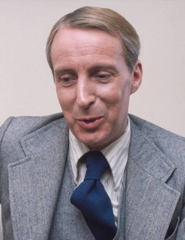 Colour photograph of Ian Richardson, a fair-haired man in a grey herringbone suit and navy tie, caught mid-sentence.