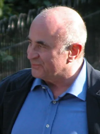 Bob Hoskins in profile outdoors, a bald man in a blue open-collar shirt and dark jacket, looking to the left.