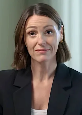 Head and shoulders photograph of a woman with a shoulder-length brown bob, gold earring and a black blazer over a white top.