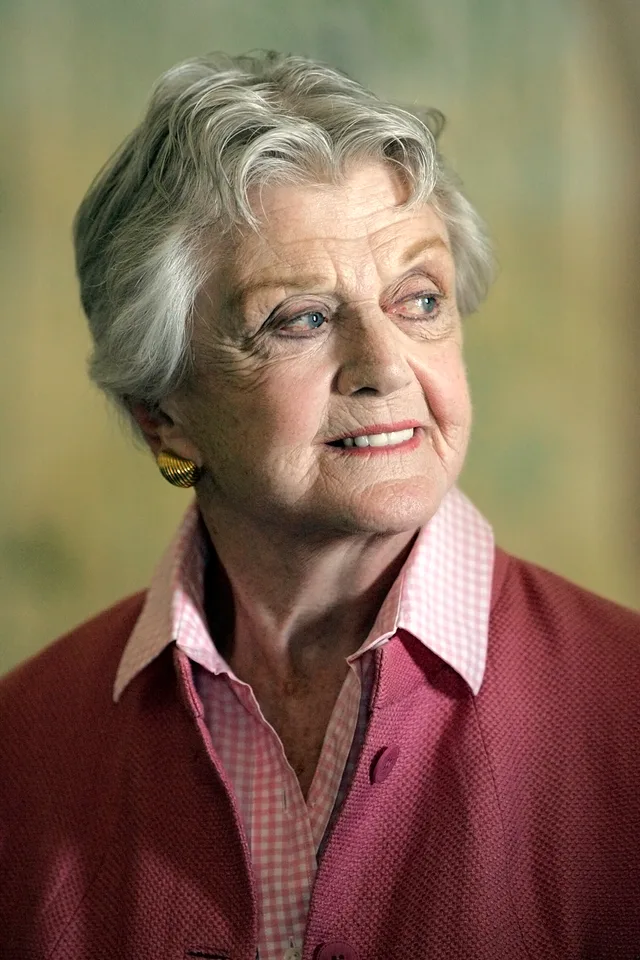 Colour portrait of an elderly woman with short grey hair, in a pink gingham collar and rose-coloured jacket, looking off to one side.