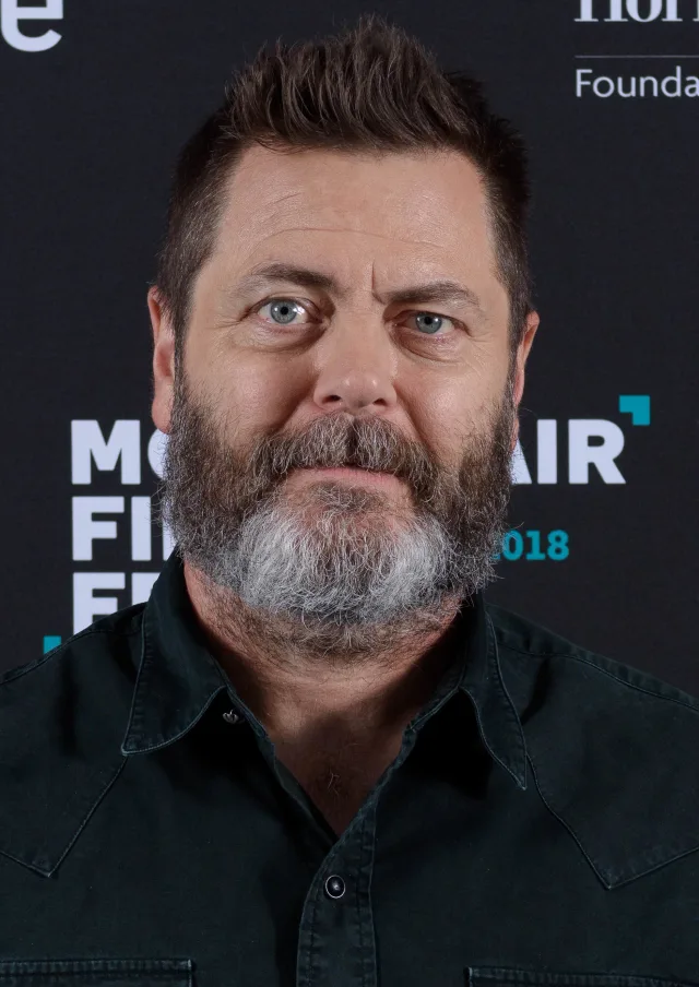 Nick Offerman facing the camera with short spiky hair and a full beard, in a dark shirt against a film festival backdrop