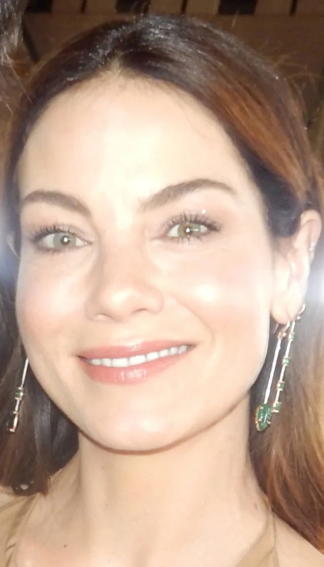 Close photograph of a smiling woman with shoulder-length brown hair and long green drop earrings.