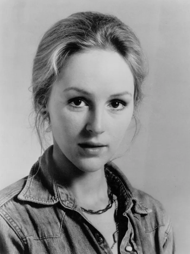 Black and white studio portrait of a young woman with her hair pinned up, wearing a denim shirt and a chain necklace.