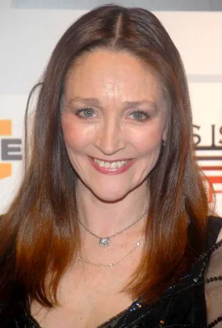 Head and shoulders photograph of Olivia Hussey smiling, with long auburn hair and a sparkling necklace, in front of an event backdrop.