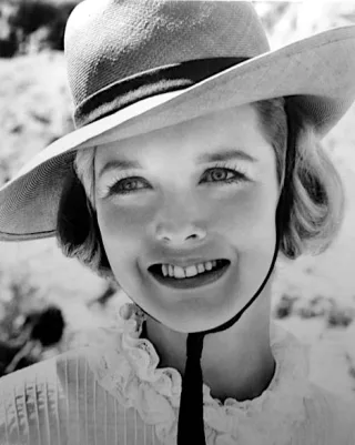 Black and white portrait of a young Barbara Babcock smiling in a wide-brimmed straw hat and a frilled pleated collar.