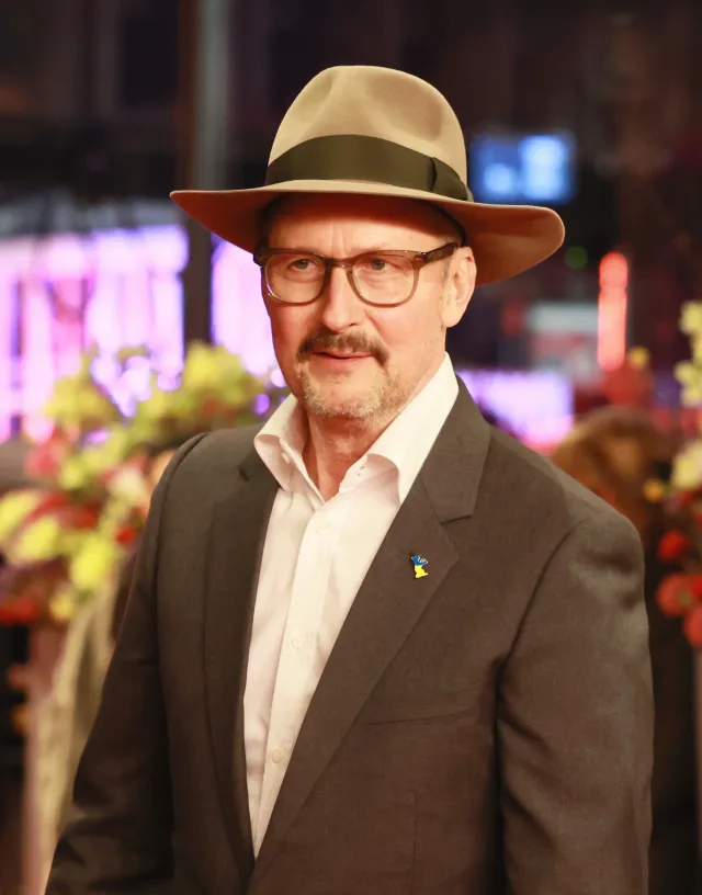 Todd Field in a brimmed hat, glasses and a grey jacket over a white open-collared shirt, photographed at an evening event.