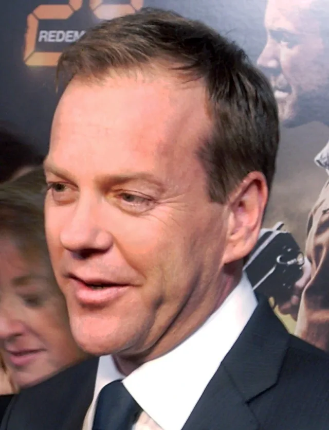Close headshot of Kiefer Sutherland in a dark suit and tie, looking to one side at a premiere.