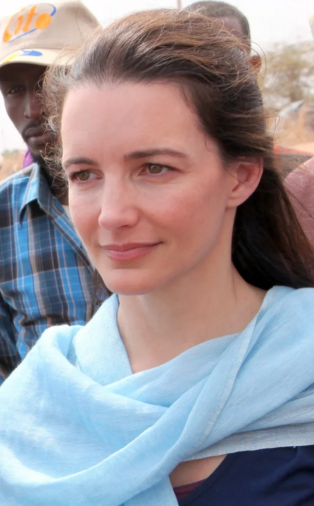 Close photograph of a woman with long dark hair pulled back, wearing a pale blue scarf, outdoors in a dry landscape.