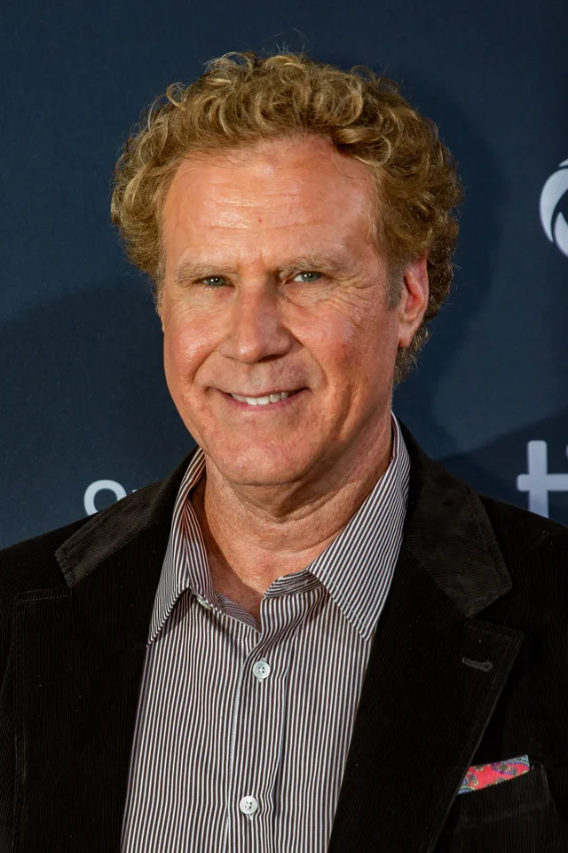 Head and shoulders photograph of a smiling man with curly fair hair, wearing a dark jacket over a striped shirt with a pink pocket square.