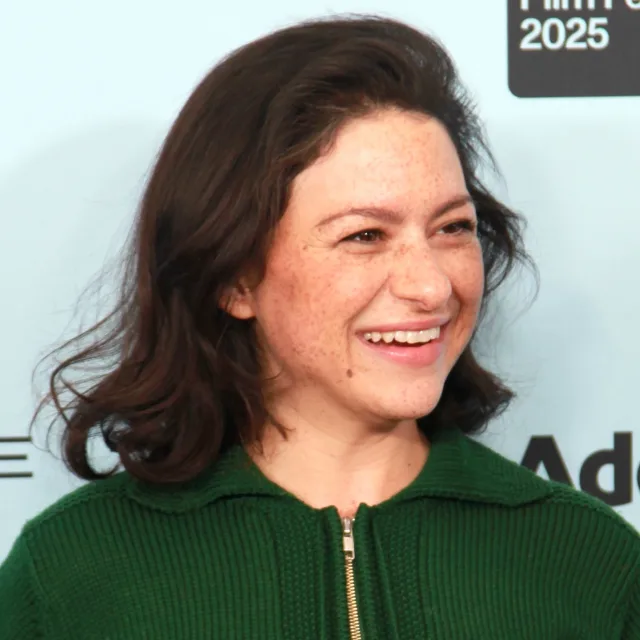 Close photograph of Alia Shawkat smiling and looking to one side, with shoulder-length dark hair and a green knit zip-neck top.