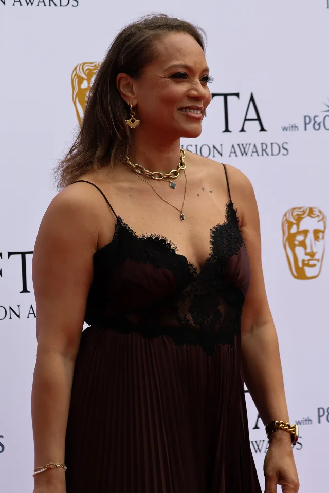 Angela Griffin smiling in profile at a television awards photocall, wearing a dark lace-trimmed dress and gold jewellery.