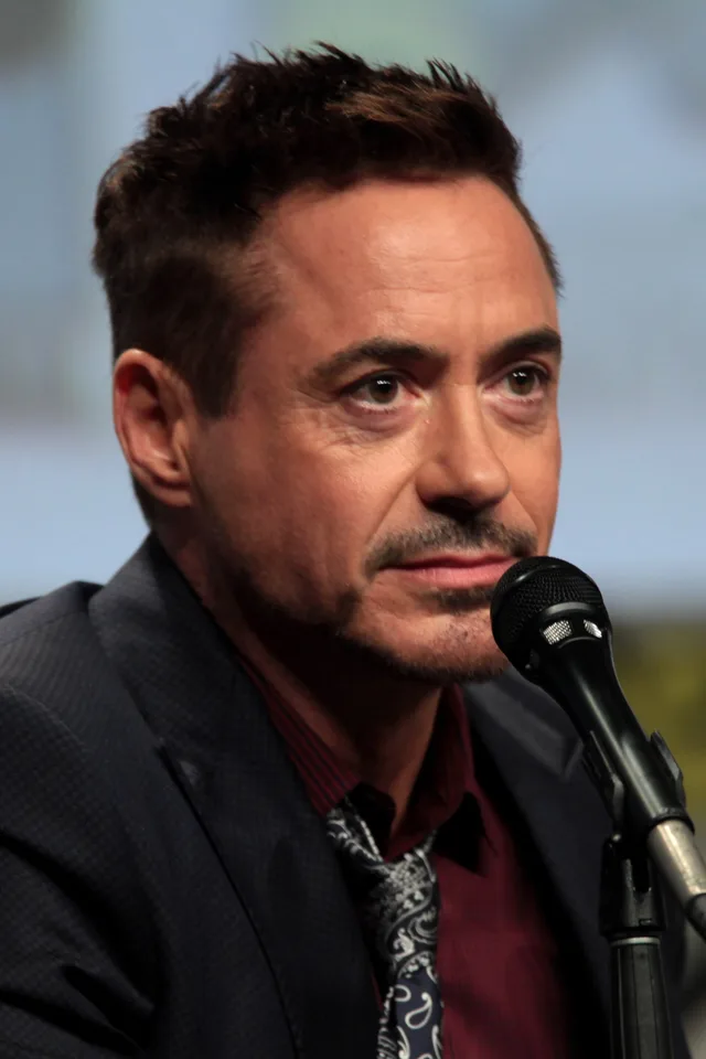 Close photograph of a man with short dark hair and a trimmed goatee, in a dark jacket and paisley tie, seated at a microphone at a convention panel.
