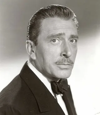 Black and white studio portrait of a middle-aged man with slicked-back hair and a moustache, wearing a dark jacket and bow tie and looking at the camera.