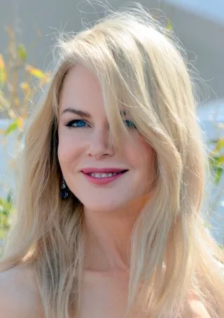 Portrait of Nicole Kidman outdoors with long blonde hair falling across her face, smiling slightly.