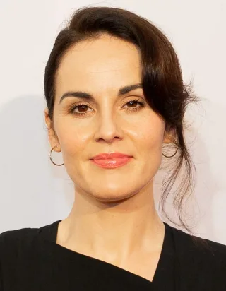 Close photograph of Michelle Dockery, a woman with dark hair pinned loosely back, wearing gold hoop earrings and a black top.