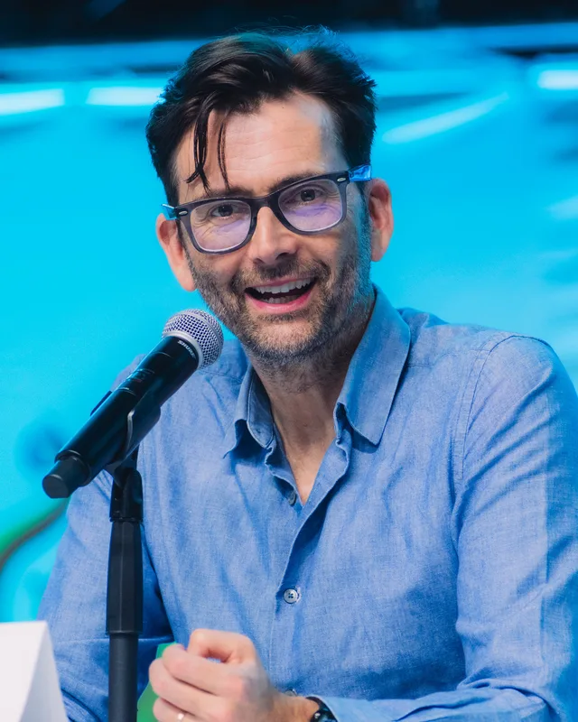 David Tennant photographed at a fan convention in 2025, a man with swept-back brown hair smiling.