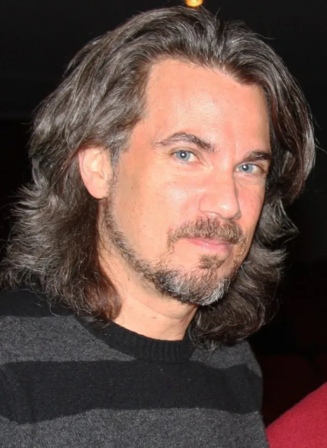 Close photograph of Robby Benson, a man with long grey-brown hair and a goatee, wearing a dark striped jumper.