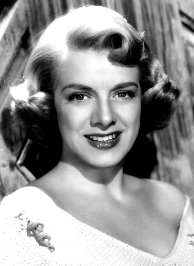 Black and white studio portrait of Rosemary Clooney smiling, with styled curled hair and an off-the-shoulder white knit top.