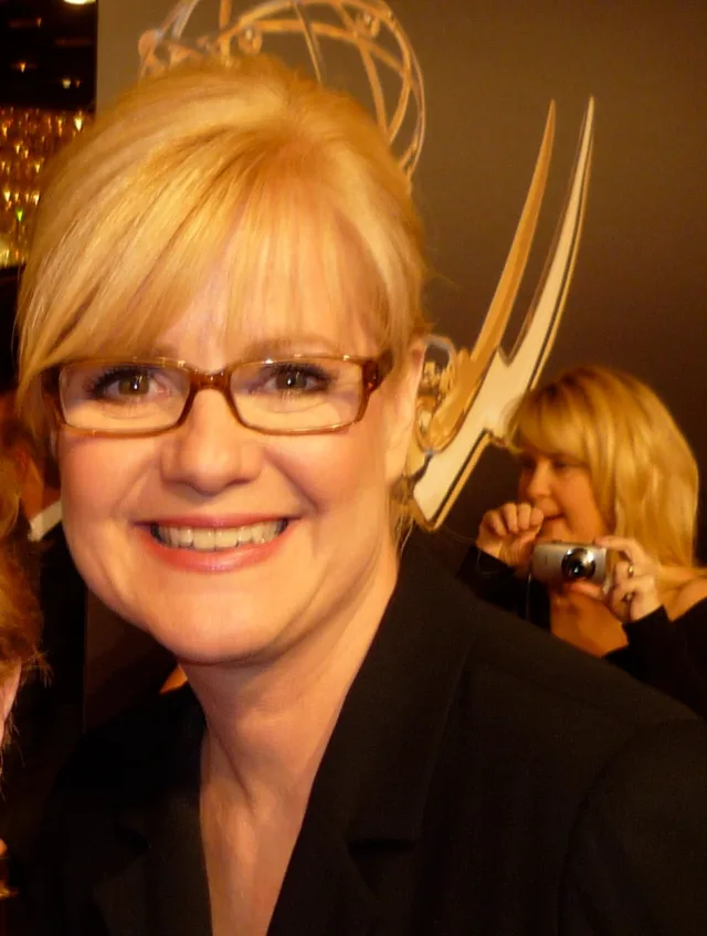 Close photograph of Bonnie Hunt smiling, with blonde hair and amber-framed glasses, wearing a dark jacket at an awards event.