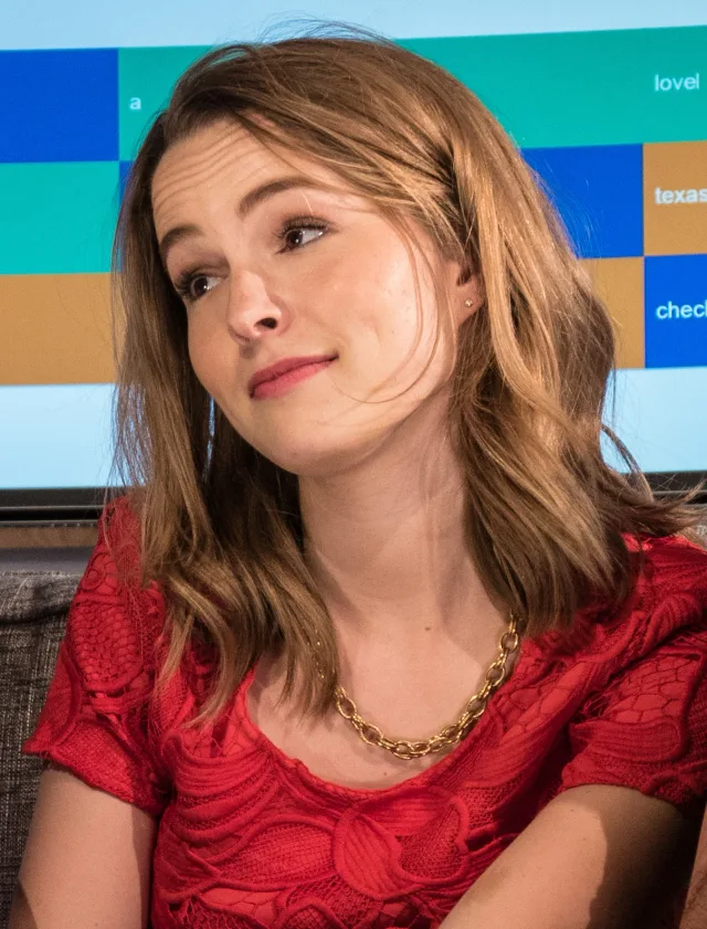 Close photograph of a young woman with shoulder-length light brown hair, wearing a red lace top, looking to one side with a slight smile.