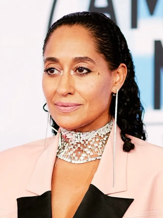Close portrait of Tracee Ellis Ross with dark braided hair, a sparkling silver choker and a pale pink jacket.