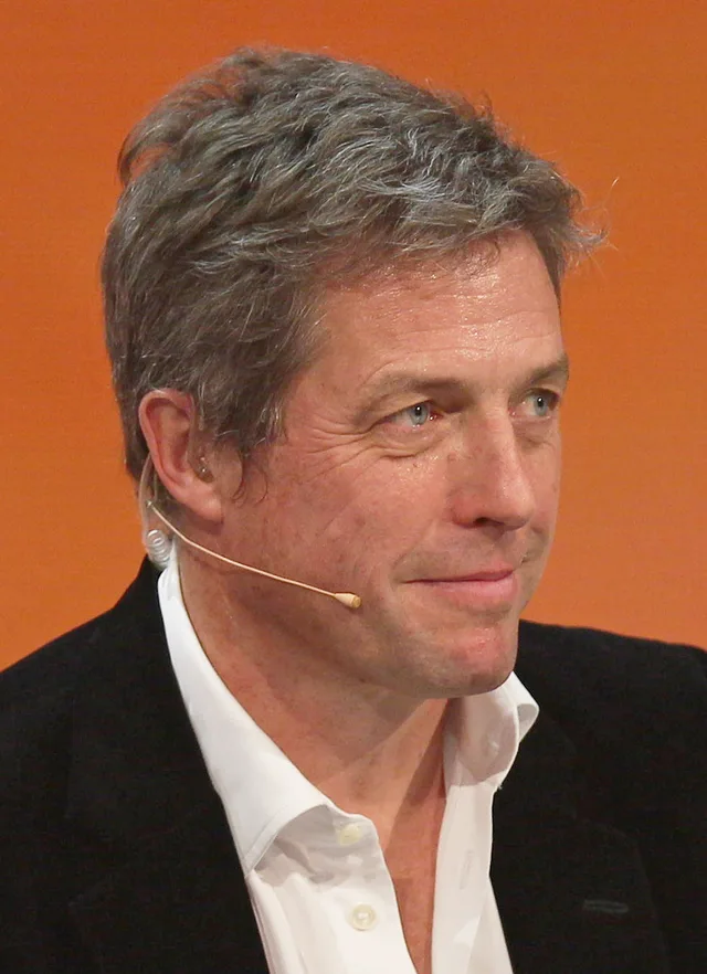 Hugh Grant photographed at a television show in Graz in 2014, smiling in a dark jacket.