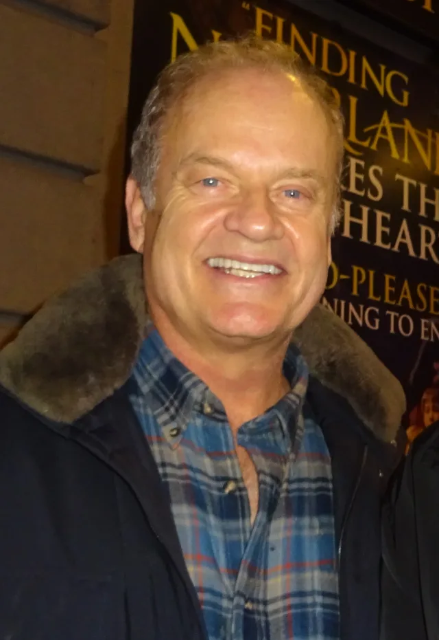 Close-up photograph of Kelsey Grammer smiling, wearing a dark fleece-collared jacket over a blue checked shirt