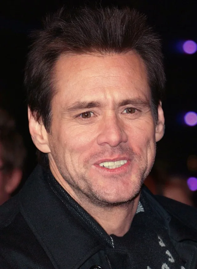 Close-up photograph of a smiling man with short dark brown hair, wearing a dark jacket, at an evening event with purple lights behind him.