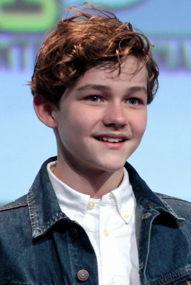 Head and shoulders photograph of a smiling young man with tousled auburn hair, wearing a denim jacket over a white button-down shirt.