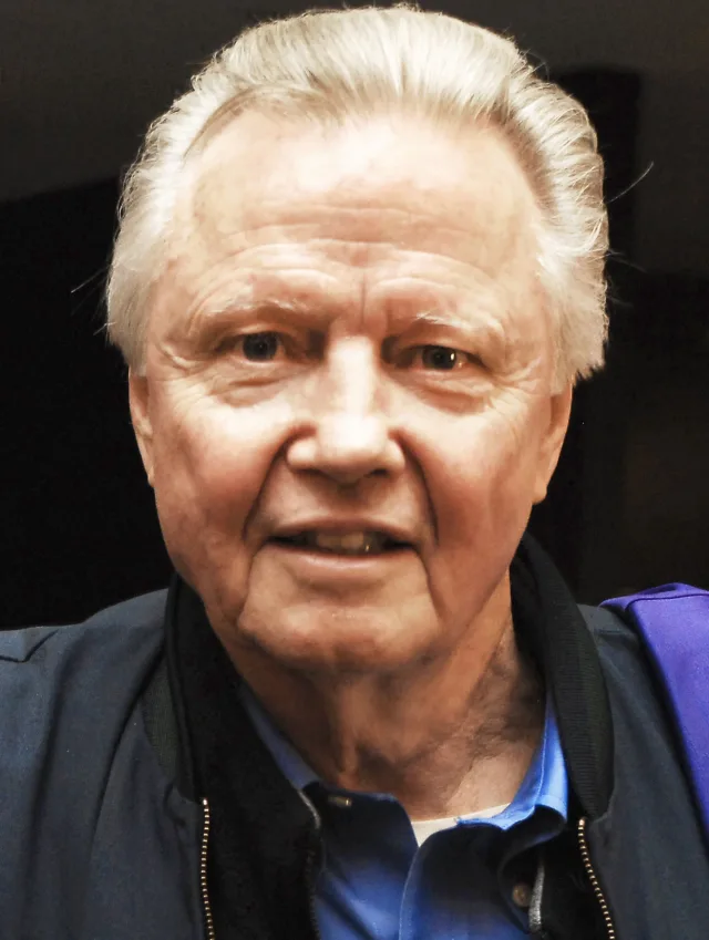 Close photograph of an older man with swept-back white hair and a faint smile, wearing a navy zip jacket over a blue polo shirt.
