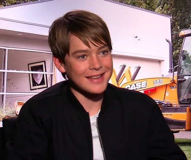 Smiling young man with brown side-swept hair and a dark zip jacket, photographed during an interview.
